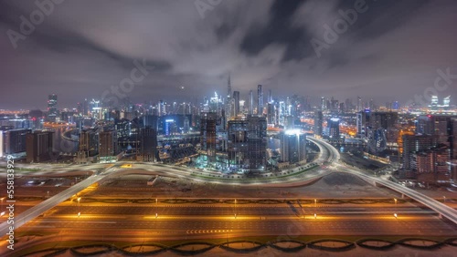 Panoramic skyline of Dubai with business bay and downtown district during all night timelapse. Aerial view of many modern skyscrapers and busy traffic on al khail road. Moon setting down and lights photo