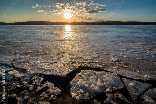 Spring cracks on the ice of the river, view at sunset. Beauty of nature.