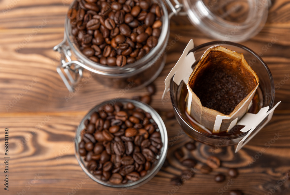 A glass cup of freshly brewed coffee with a handy drip coffee filter on a brown wooden background. Making freshly brewed coffee at home. Copyspace. Place for text.Coffee making concept. A glass cup of freshly brewed coffee with a handy drip coffee filter on a brown wooden background. Making freshly brewed coffee at home. Copyspace. Place for text.Coffee making concept.