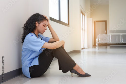 A tired female nurse in a blue uniform sits on the hospital floor. sad feeling exhausted from stress © atitaph