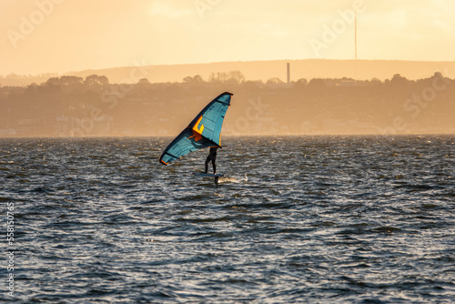 windsurfer at Hill Head Hampshire England with the Isle of Wight and an orange haze from the sun setting in the background © Penny