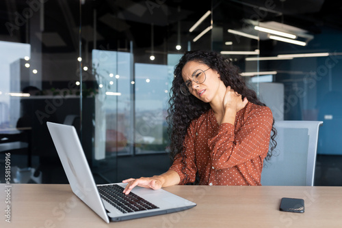 Canvastavla Overtired business woman working inside office with laptop, Hispanic female worker has severe neck pain, massaging muscles with hand