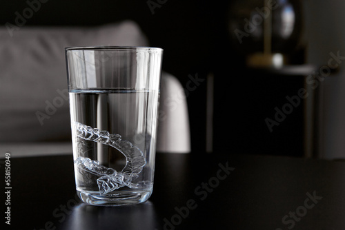 Transparent invisible orthodontic tooth aligners, retainers cleaning in a glass with water on a table in apartment
