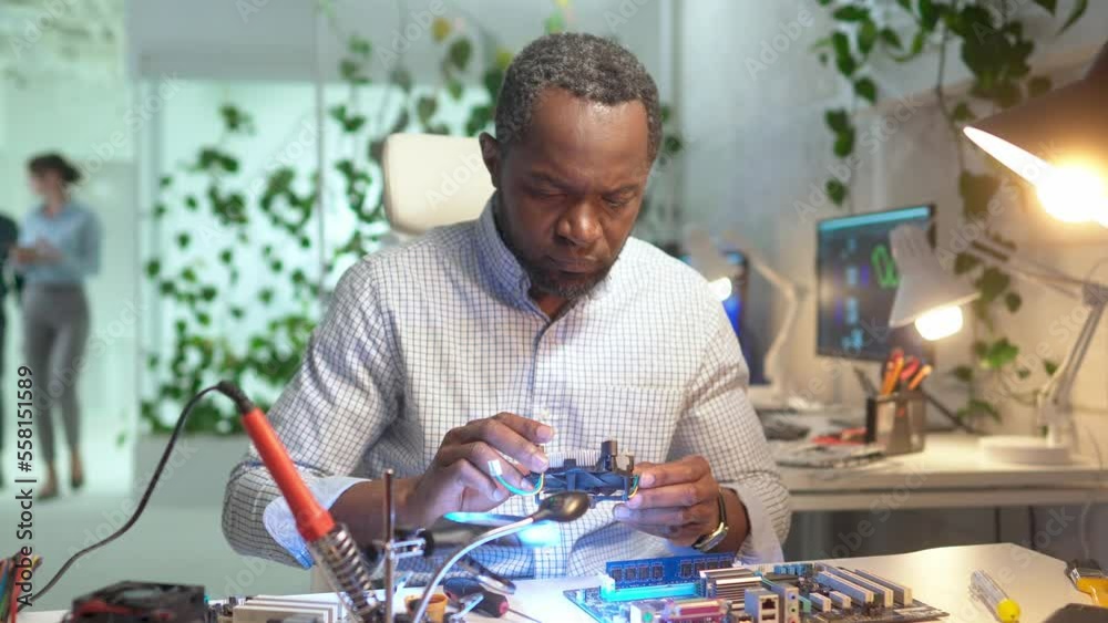 Portrait of focused professional young man working in service setting up cooler on motherboard. Concentrated African engineer repairing computer sitting in modern office using tools.