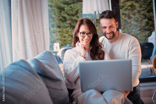 Happy couple using laptop while relaxing on the sofa at home