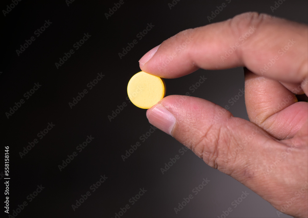 Man holding a yellow pill or tablet medicine with two fingers. Close up. Man holding a yellow pill or tablet medicine with two fingers. Close up.