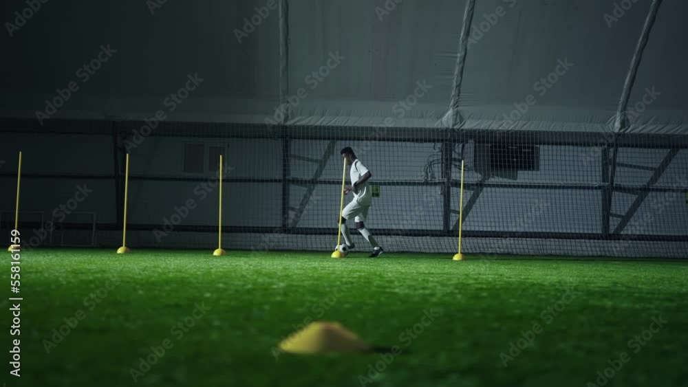 junior african football player training in hall, running with ball between sticks