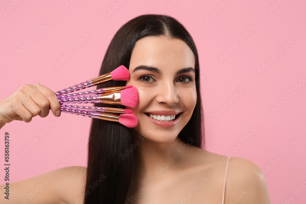 Happy woman with different makeup brushes on pink background Happy woman with different makeup brushes on pink background