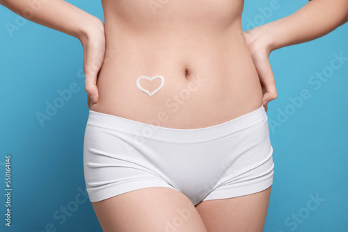 Woman with heart made of body cream on her belly against light blue background, closeup © New Africa