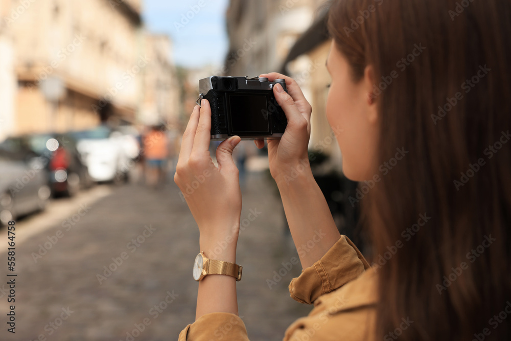 Young woman with camera taking photo on city street, space for text. Interesting hobby