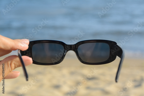 Woman holding stylish sunglasses near beautiful sea, closeup