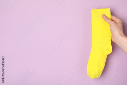 Woman holding yellow sock on light violet background, closeup. Space for text