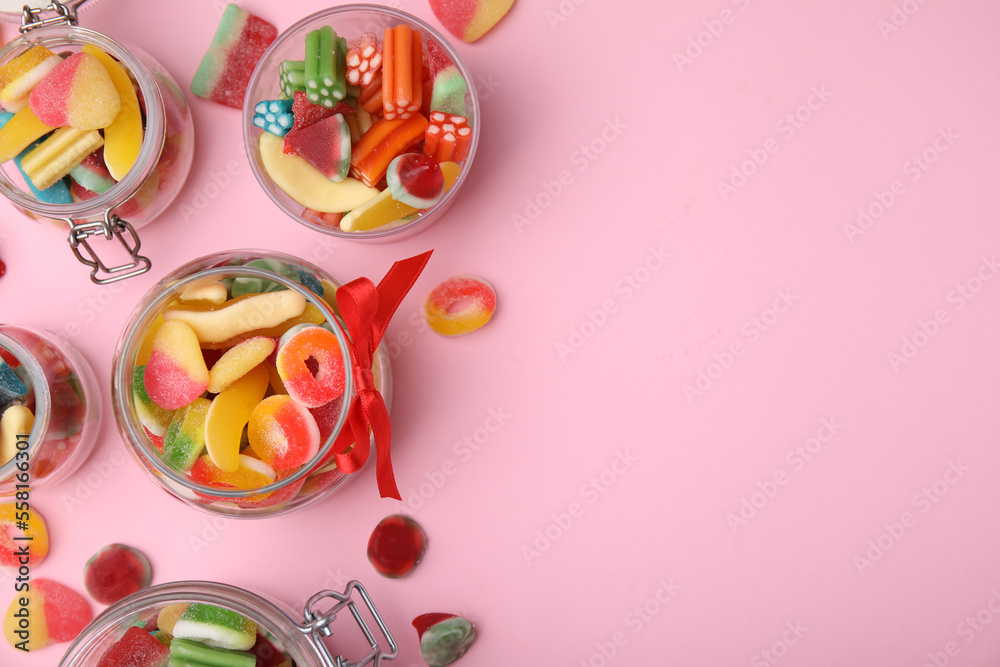 Glass jars with tasty colorful jelly candies on pink background, flat lay. Space for text