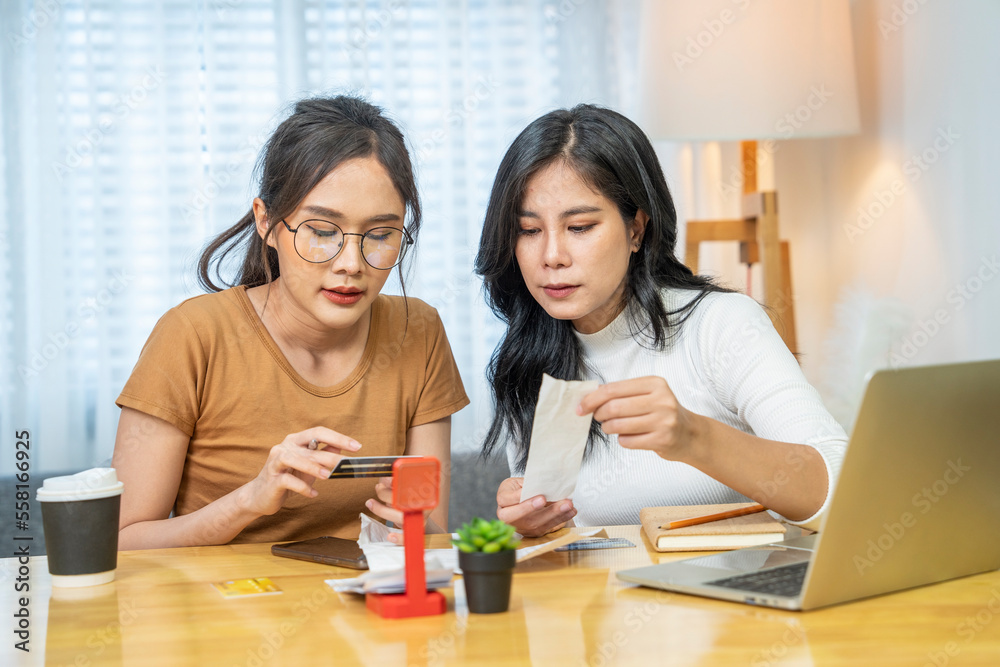 Asian sisters looking at bills and credit card invoices due for billing invoices using credit card payment via smartphone application to pay bills with at home Asian sisters looking at bills and credit card invoices due for billing invoices using credit card payment via smartphone application to pay bills with at home