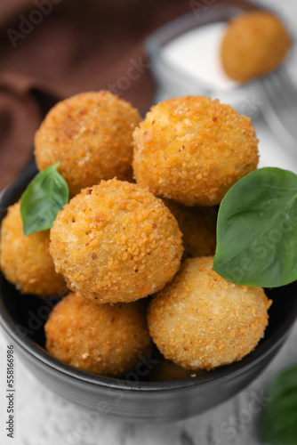 Bowl of delicious fried tofu balls with basil on textured table, closeup