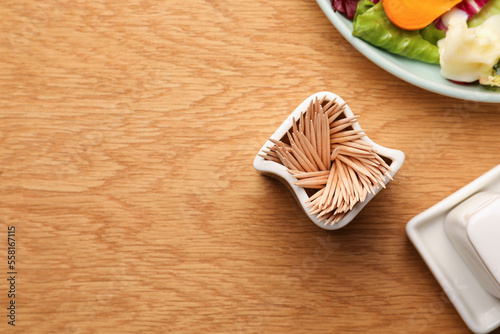 Holder with many toothpicks near food on wooden table, flat lay. Space for text