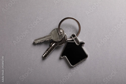 Keys with trinket in shape of house on grey background, top view. Real estate agent services