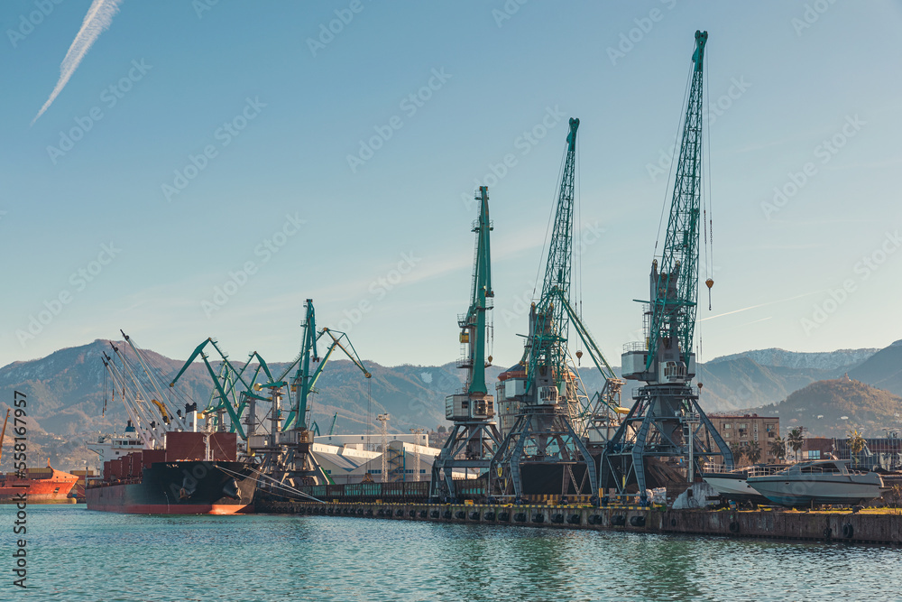 Cranes at sea port with a boat at rest is loading with cargo for import. Logistic or transportation concept