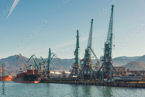 Cranes at sea port with a boat at rest is loading with cargo for import. Logistic or transportation concept
