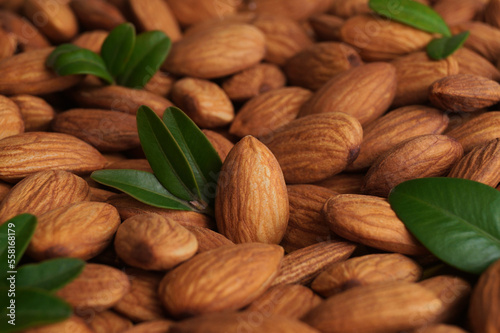Many delicious almonds and fresh leaves as background, closeup