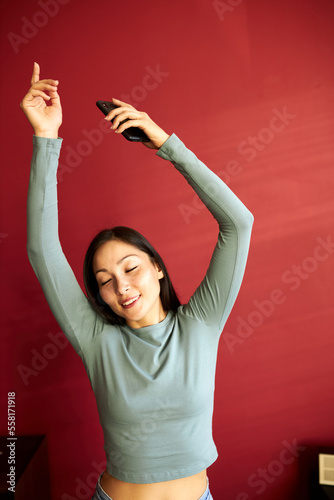 Inspired and animated dance of a girl with closed eyes against a red wall. Beautiful lady looking at the camera, close up portrait