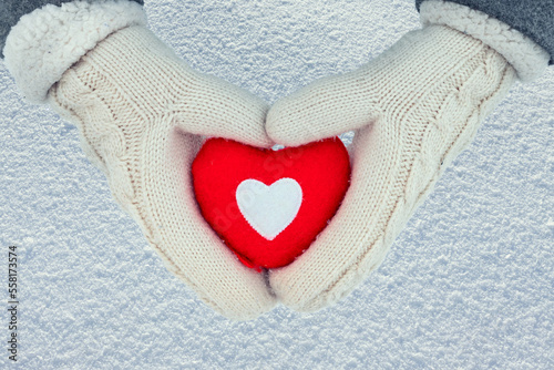 Red heart in woman s hands wearing white woolen mittens. Top view snow background  Valentine s Day concept