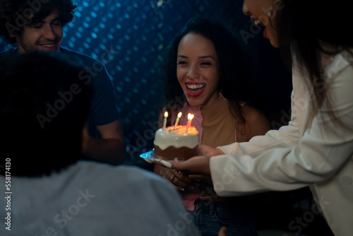 Beautiful young woman shocked and excited on receiving a small cake with candles for housewarming and birthday with friends at midnight during party at home