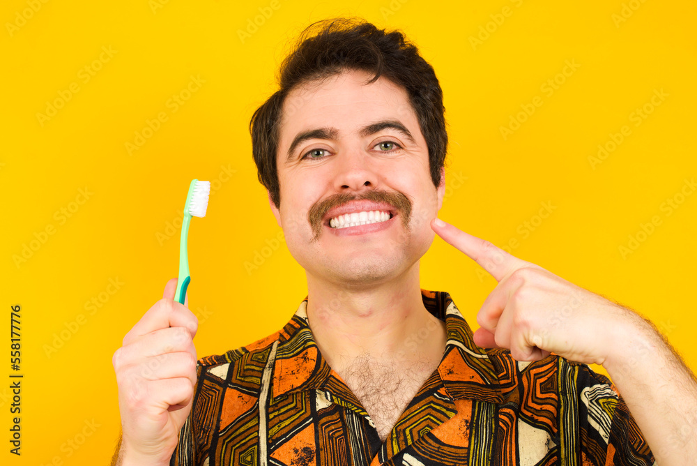 Handsome man standing over yellow studio background brushing his teeth. Dental healthcare concept. Handsome man standing over yellow studio background brushing his teeth. Dental healthcare concept.