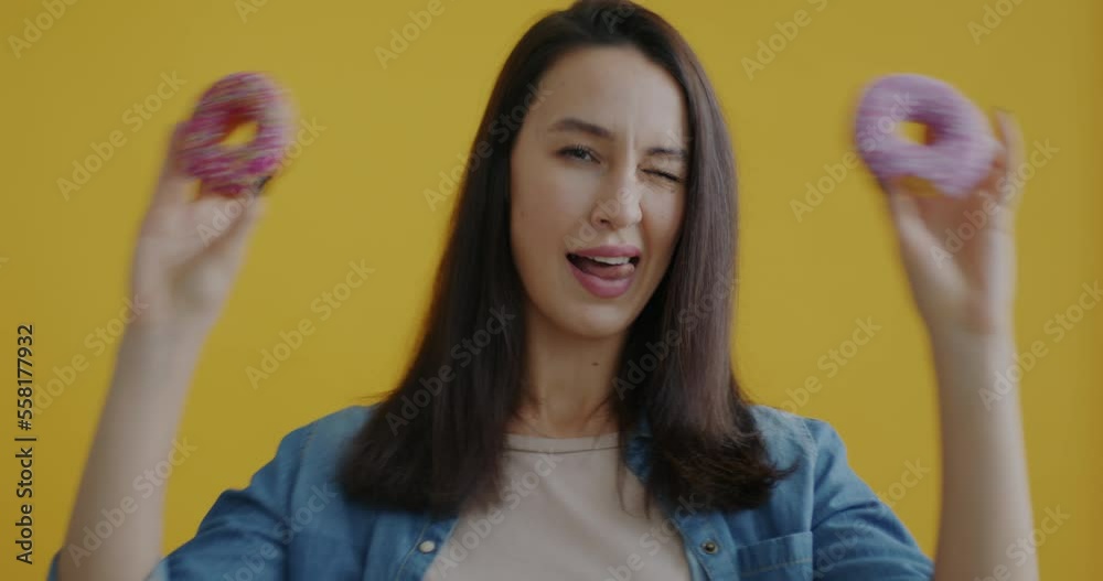 Portrait of attractive young lady playing with donuts and making cute faces on yellow background. Delicious dessert and people concept. Portrait of attractive young lady playing with donuts and making cute faces on yellow background. Delicious dessert and people concept.
