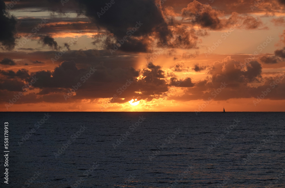 Dramatic sunset over ocean with tiny sailing boat