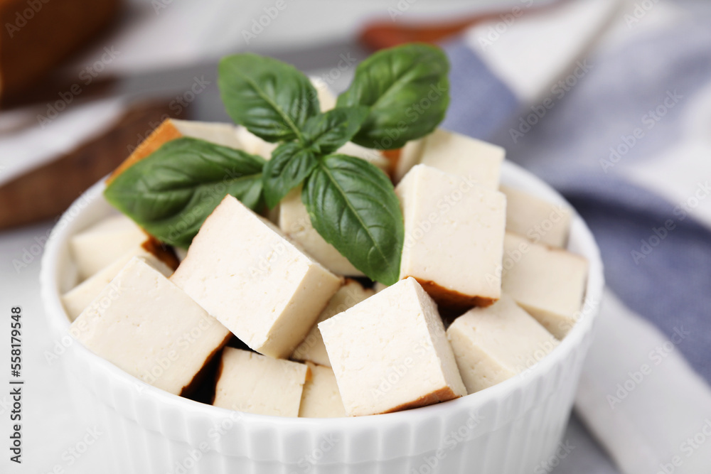 Bowl of smoked tofu cubes with basil on table, closeup