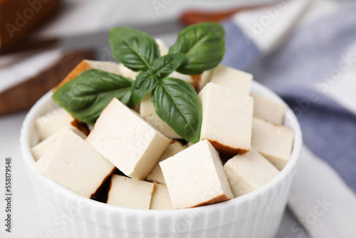 Bowl of smoked tofu cubes with basil on table, closeup