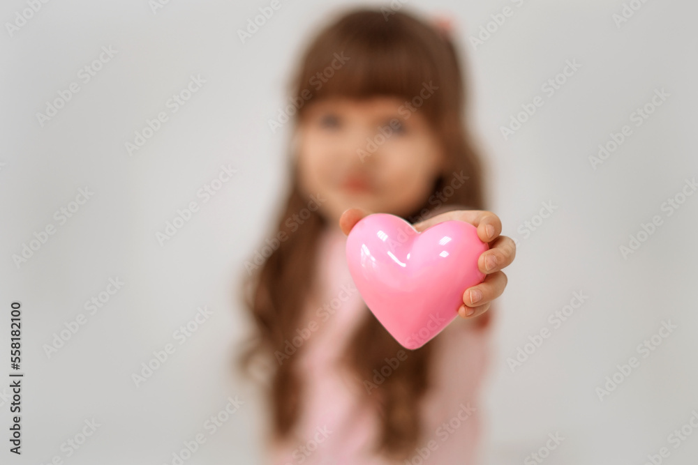 Little cute girl holds a pink heart in his hand stands on a white background. Copy space. Soft focus. Little cute girl holds a pink heart in his hand stands on a white background. Copy space. Soft focus.