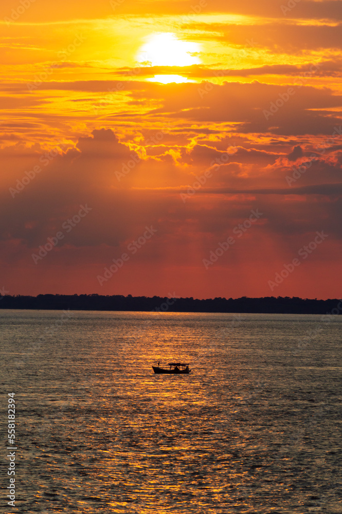 Sunrise on the Amazon river in Brazil, a small boat sails in the reflection of the sunlight on the water 