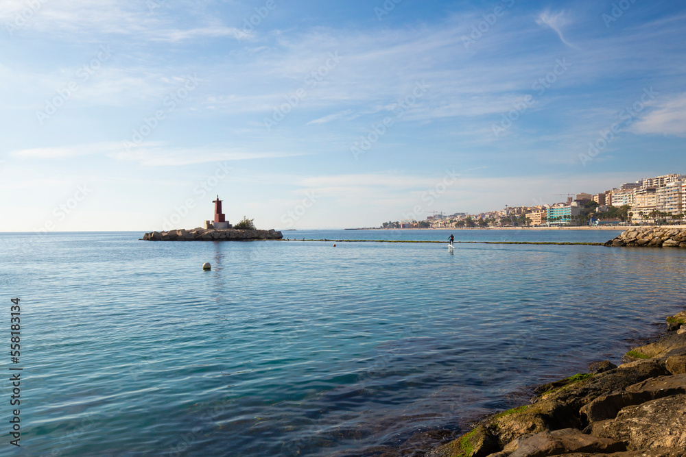The coast of the Mediterranean Sea in the resort town with a view of the lighthouse in the sea and the embankment, the province of Alicante, Villajoyosa, Costa Blanca, Spain