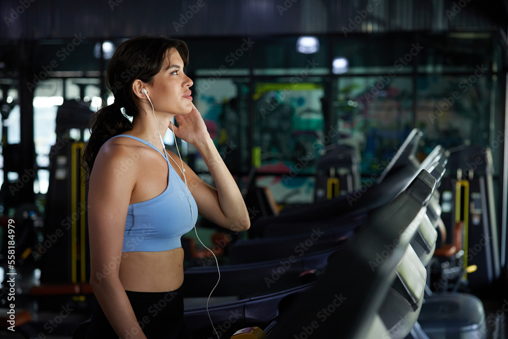young sports woman working out with wired earbuds and running on treadmill in gym