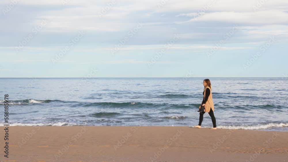 Relaxed woman walking on the beach with her shoes in her hand Relaxed woman walking on the beach with her shoes in her hand
