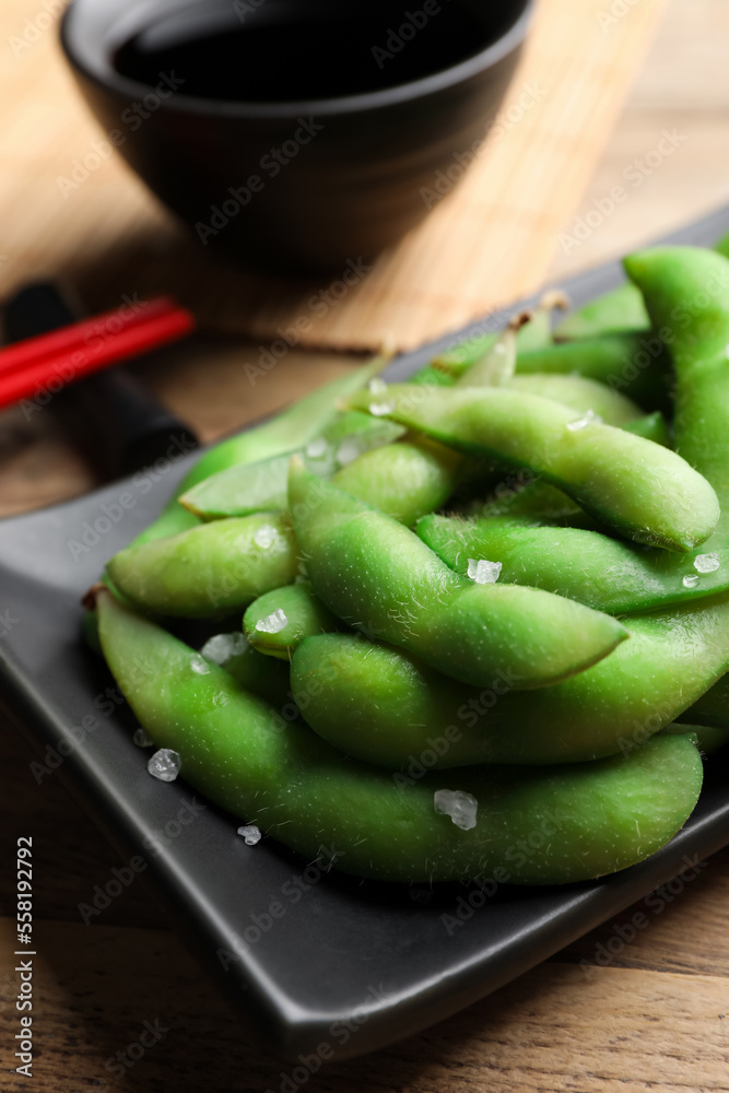 Black plate with green edamame beans in pods on wooden table, closeup Black plate with green edamame beans in pods on wooden table, closeup
