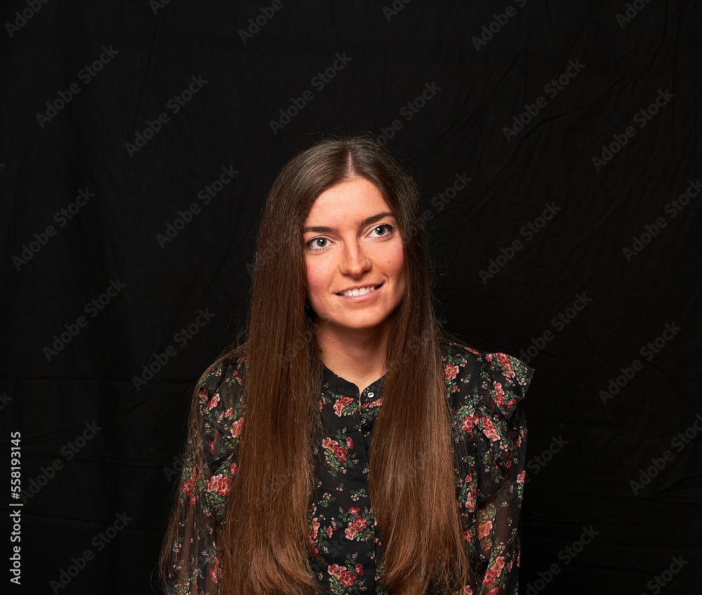 smiling girl in a black shirt with a flower print and long hair poses on a black cloth in the background smiling girl in a black shirt with a flower print and long hair poses on a black cloth in the background