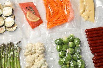Different food products in vacuum packs on white wooden table, flat lay