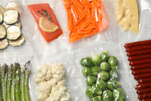 Different food products in vacuum packs on white wooden table, flat lay