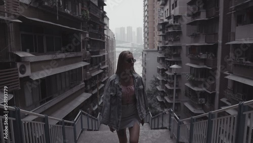 Blond hair women wearing sunglasses walking up the stairs with urban cityscape in the background, Asian densely build megapolis, Chongqing city China, Cyberpunk cityscapes, 4K stock footage