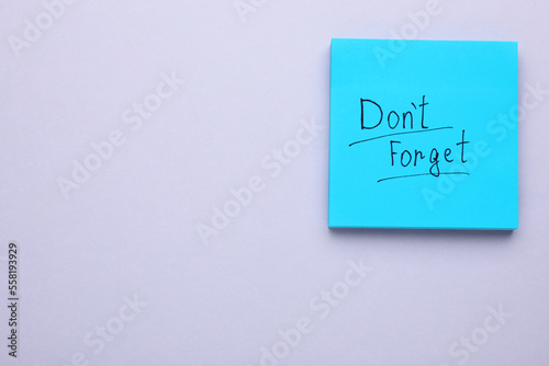 Paper note with phrase Don't Forget on light grey background, top view. Space for text