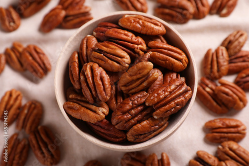 Tasty pecan nuts with bowl on beige cloth, flat lay