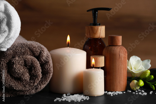 Beautiful spa composition with different care products and burning candles on black table
