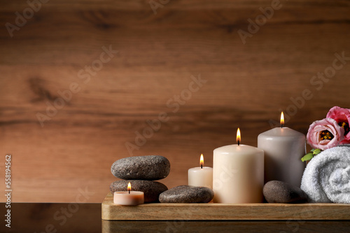 Beautiful composition with spa stones, flowers and burning candles on mirror table against wooden background. Space for text