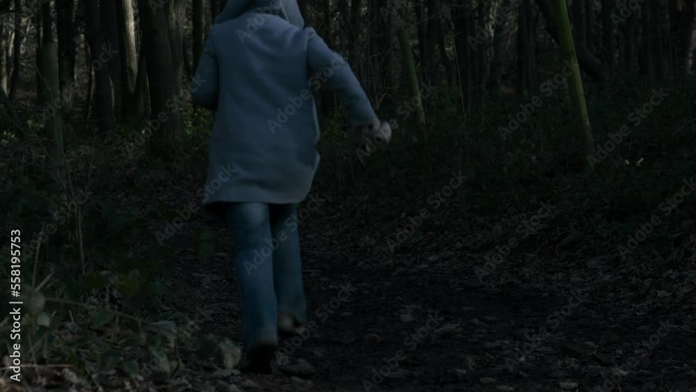 Frightened woman running through dark woodland 
