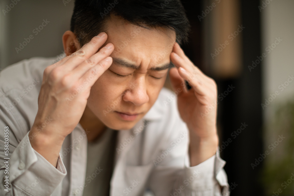 Closeup of asian middle aged man suffering from headache, touching his temples, sitting with closed eyes, copy space Closeup of asian middle aged man suffering from headache, touching his temples, sitting with closed eyes, copy space