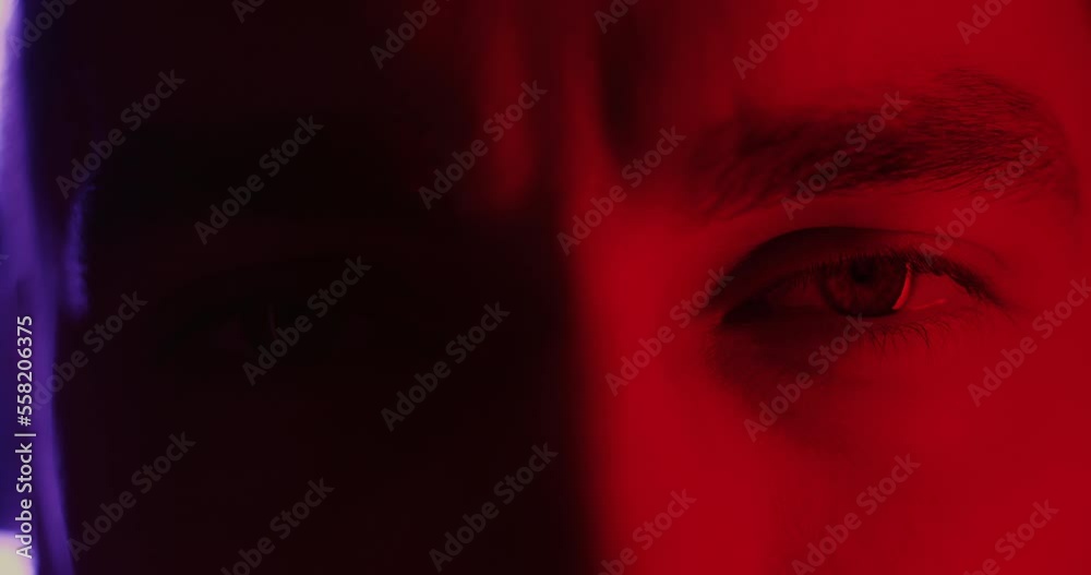 Close-up of beautiful male eyes looking at camera on flashing neon light background. Human expression and futuristic millennials concept.