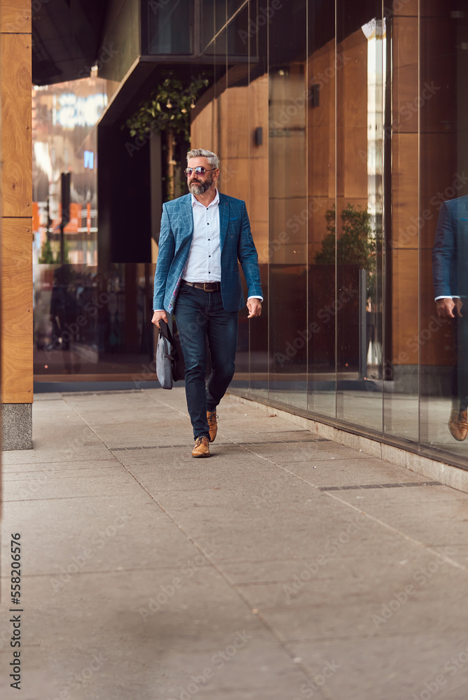 A senior businessman in a blue suit with a briefcase walking through the city A senior businessman in a blue suit with a briefcase walking through the city